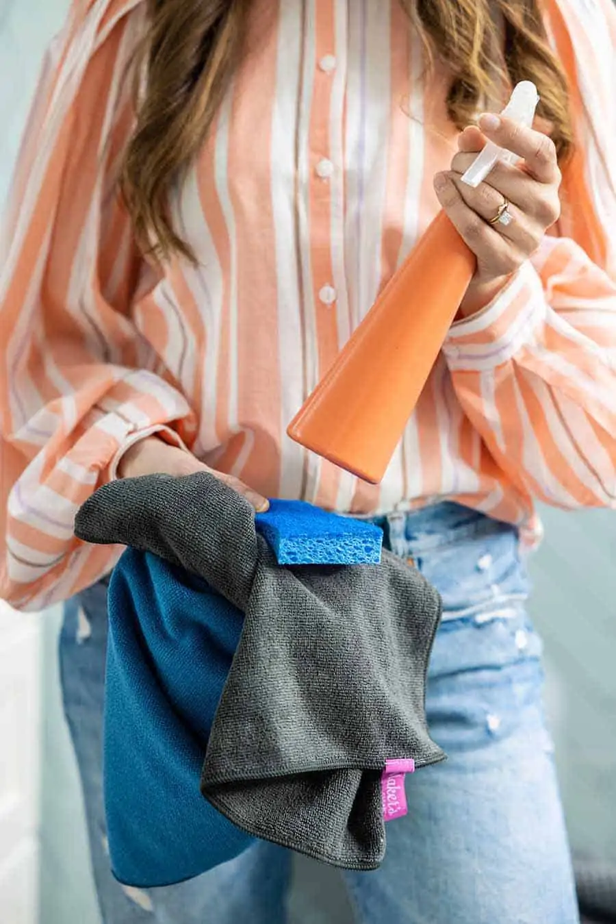 Melissa Maker holding spray bottle, sponge, and microfiber cloth. 